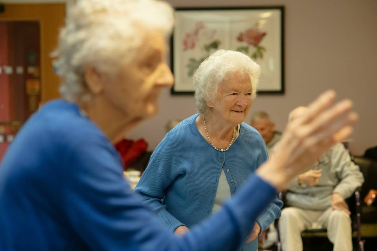 benefits of senior living communities: modern, light-filled common area with seniors chatting over coffee and accessible garden pathways visible through floor-to-ceiling windows